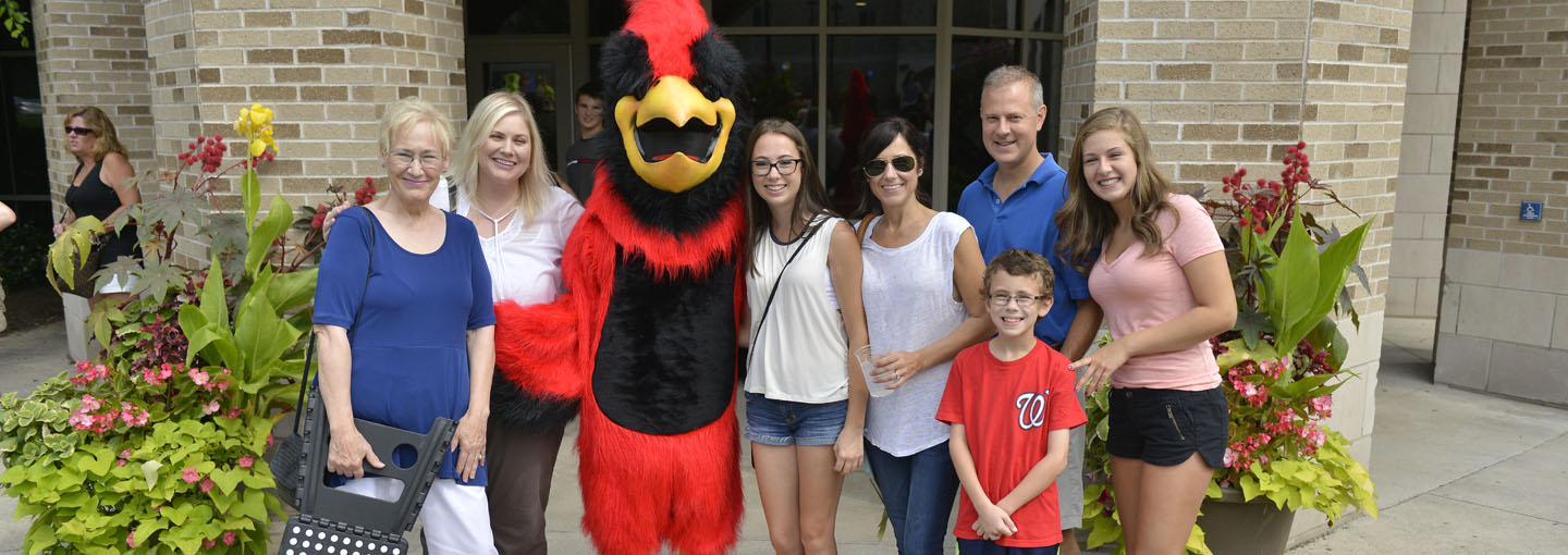 Family poses for camera with Cardinal in front of Campus Center.