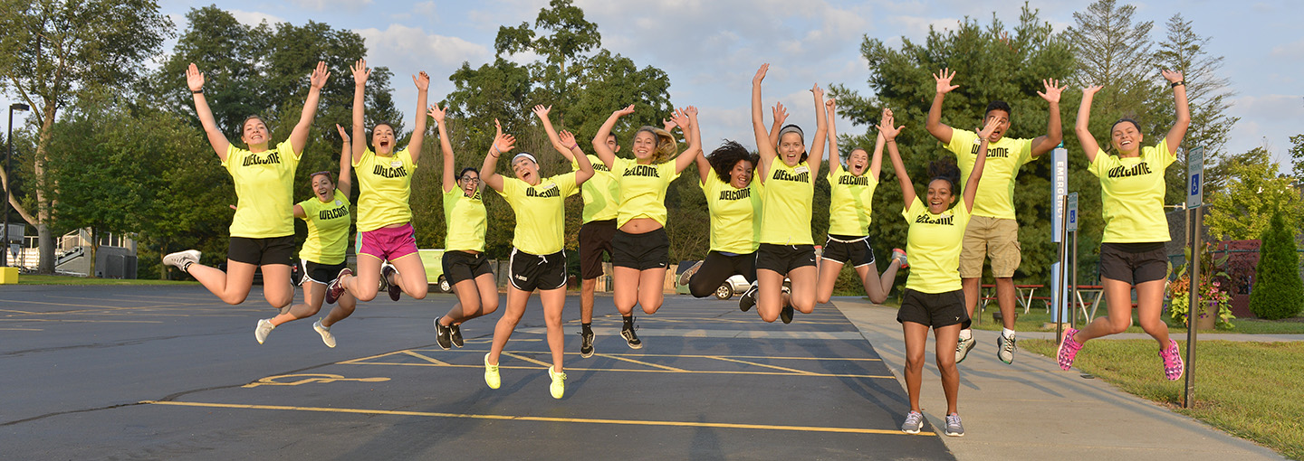 Orientation leaders in matching welcome t-shirts jump in the air.