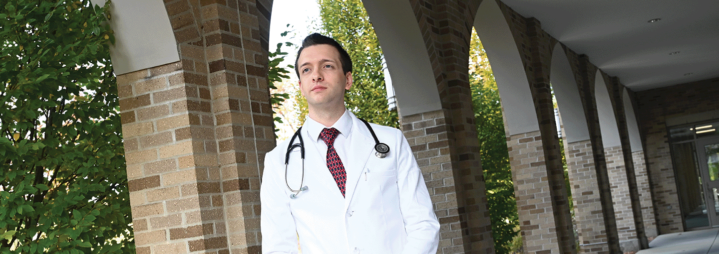 A graduate nursing student stands confidently with a stethoscope draping his shoulders.