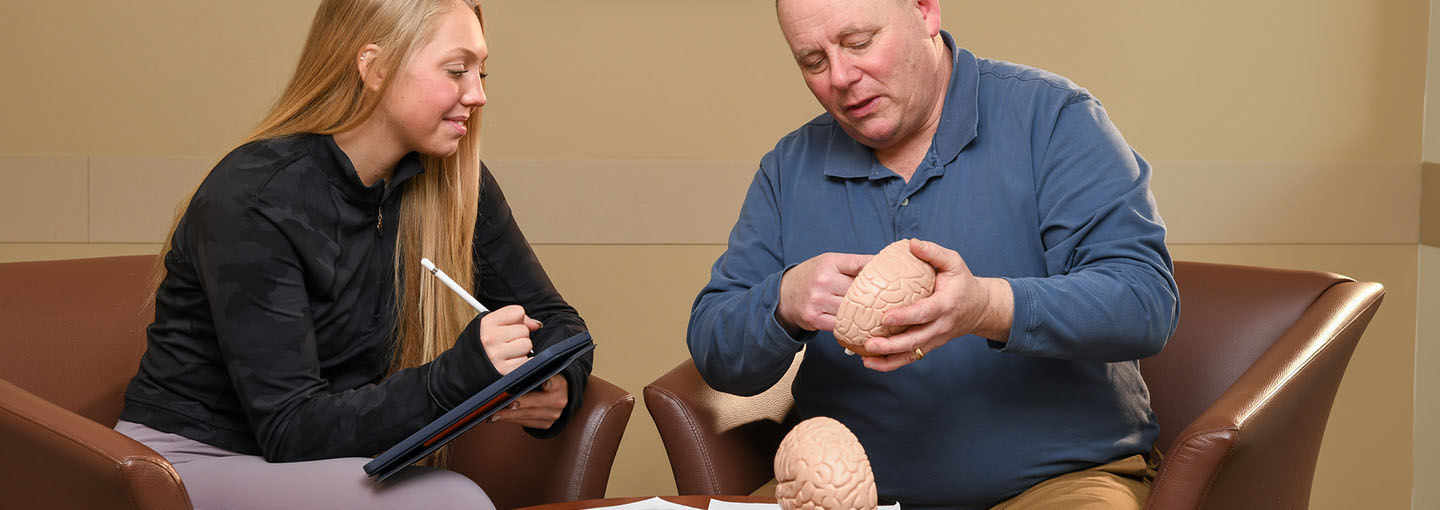 A student with a psychology professor observing a model human brain.