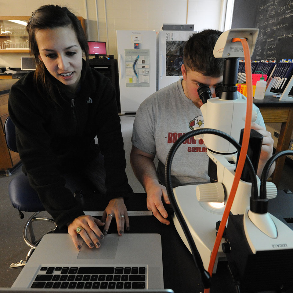 Students at laptop and microscope in science lab.